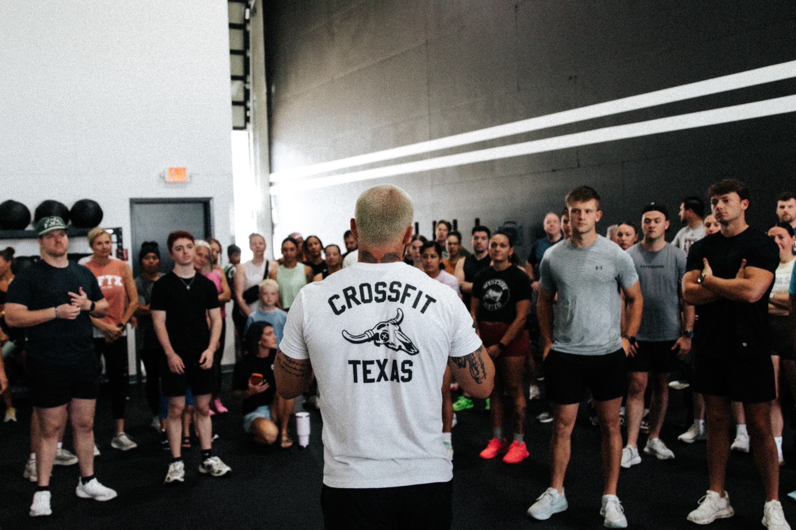 A CrossFit Texas coach in a branded tee addressing a full class on the gym floor